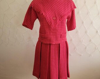 May include: A pink and white checkered vintage dress with a short-sleeved jacket and a fringe collar. The dress has a pleated skirt.