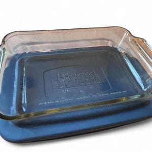 Puede incluir: Una fuente de horno rectangular de vidrio transparente con asas integradas. La base tiene grabado el logotipo de Anchor Hocking, las dimensiones de 20 cm x 28 cm y una capacidad de 2 L. El vidrio es transparente con bordes redondeados.
