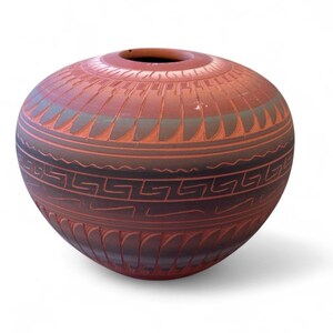 May include: A round terracotta-colored clay vessel featuring a wide opening at the top. The exterior surface is decorated with dark brown horizontal bands, intricate geometric Greek key patterns, and repeating feather-like motifs in relief.