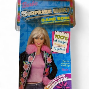 May include: A Barbie Surprize Ink game book in original packaging. The blue card features a blonde doll wearing a pink shirt and a dark jacket with floral patterns and pink faux fur trim. Text includes 100's of images Magically appear!