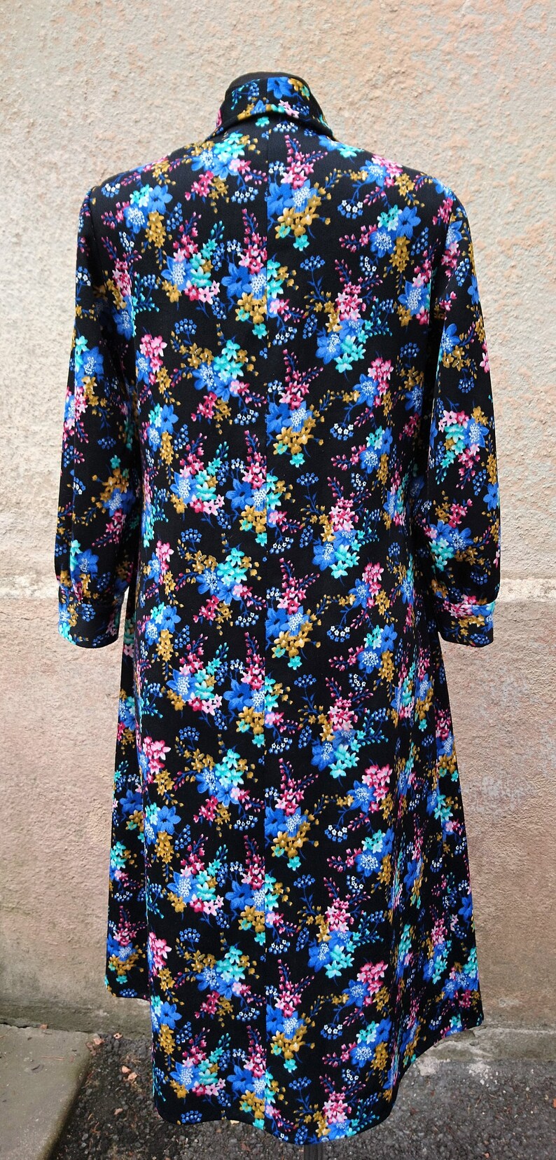 May include: A black dress with a floral print featuring blue, pink, and gold flowers. The dress has a long sleeve and a collar.