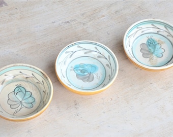 Könnte beinhalten: Drei kleine, runde Keramikschalen mit einem hellblauen und grauen Blumendesign. Die Schalen haben einen weißen Hintergrund mit einem hellblauen Rand und einem goldenen Rand.