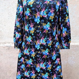 May include: A black dress with a floral print featuring blue, pink, and gold flowers. The dress has a long collar and a zipper closure.