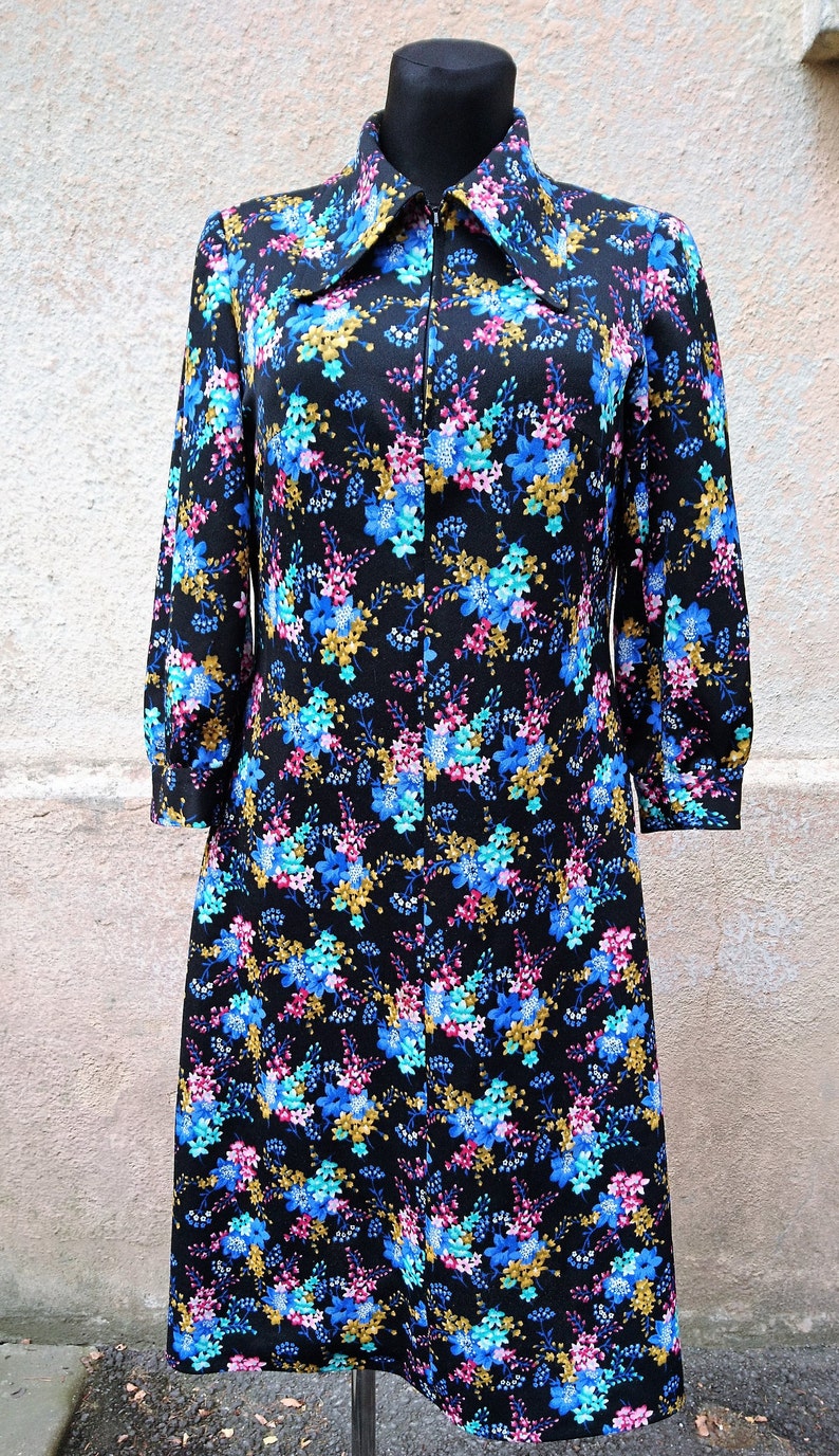 May include: A black dress with a floral print featuring blue, pink, and gold flowers. The dress has a long collar and a zipper closure.
