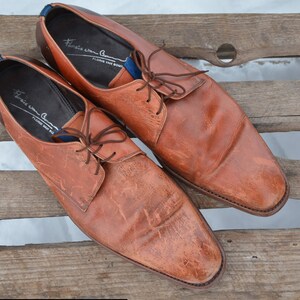 May include: A pair of brown leather lace-up shoes with a pointed toe. The shoes have a blue and white label on the inside that reads "Franco Cuomo, Florence Made in Italy".