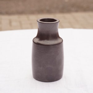 Może przedstawiać: Mały, ciemnoszary ceramiczny wazon o zaokrąglonym korpusie i lekko rozszerzonym otworze.