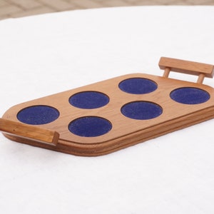 May include: Wooden tray with six blue felt-lined circles for holding glasses or cups. The tray has a handle on each side.