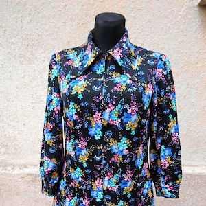 May include: A black long-sleeved dress with a large collar and a zipper closure. The dress is covered in a floral print with blue, pink, and yellow flowers on a black background.