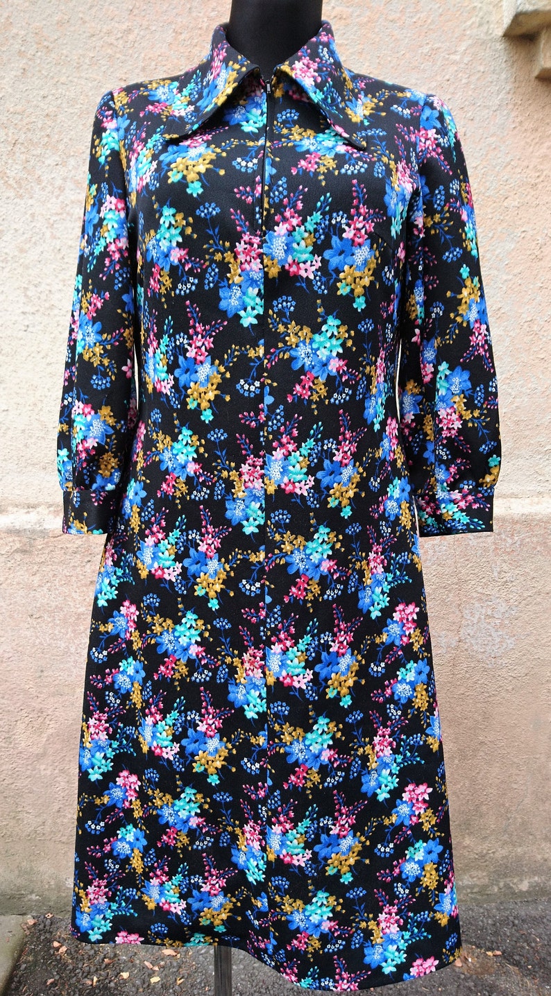 May include: A black dress with a floral print in shades of blue, pink, and gold. The dress has a long zipper down the front and a collar.