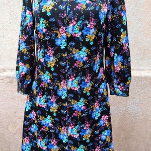May include: A black dress with a floral print featuring blue, pink, and gold flowers. The dress has a long collar and a zipper closure.