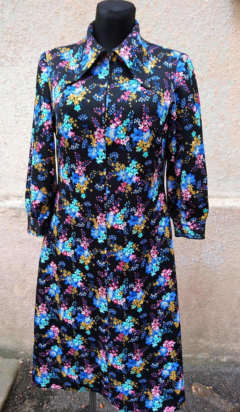 May include: A black dress with a floral print featuring blue, pink, and gold flowers. The dress has a long collar and a zipper closure.