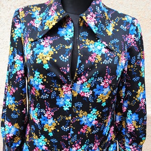 May include: A black long-sleeved dress with a floral print featuring blue, pink, and gold flowers. The dress has a zipper closure and a collared neckline.