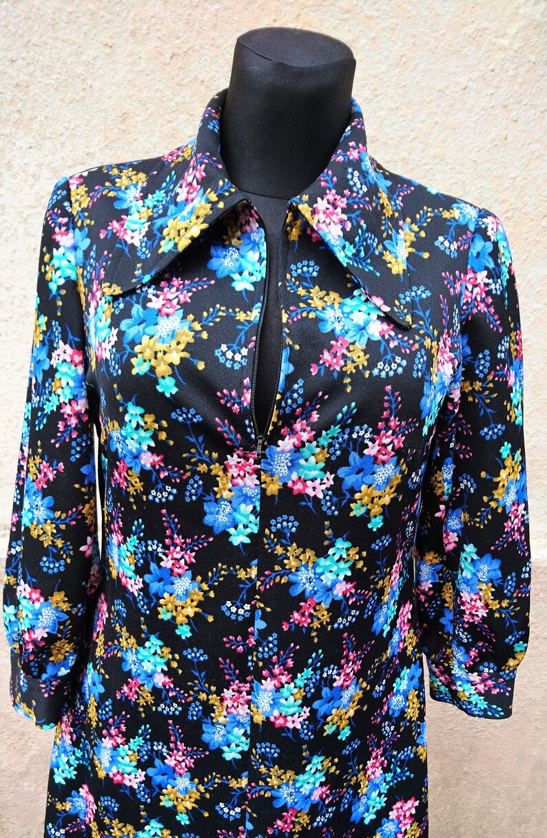 May include: A black long-sleeved dress with a floral print featuring blue, pink, and gold flowers. The dress has a zipper closure and a collared neckline.