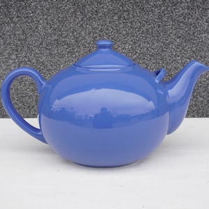 Könnte beinhalten: Eine solide blaue Teekanne aus Keramik mit einem runden Körper und einem Deckel. Die Teekanne hat einen Griff und einen Ausguss.