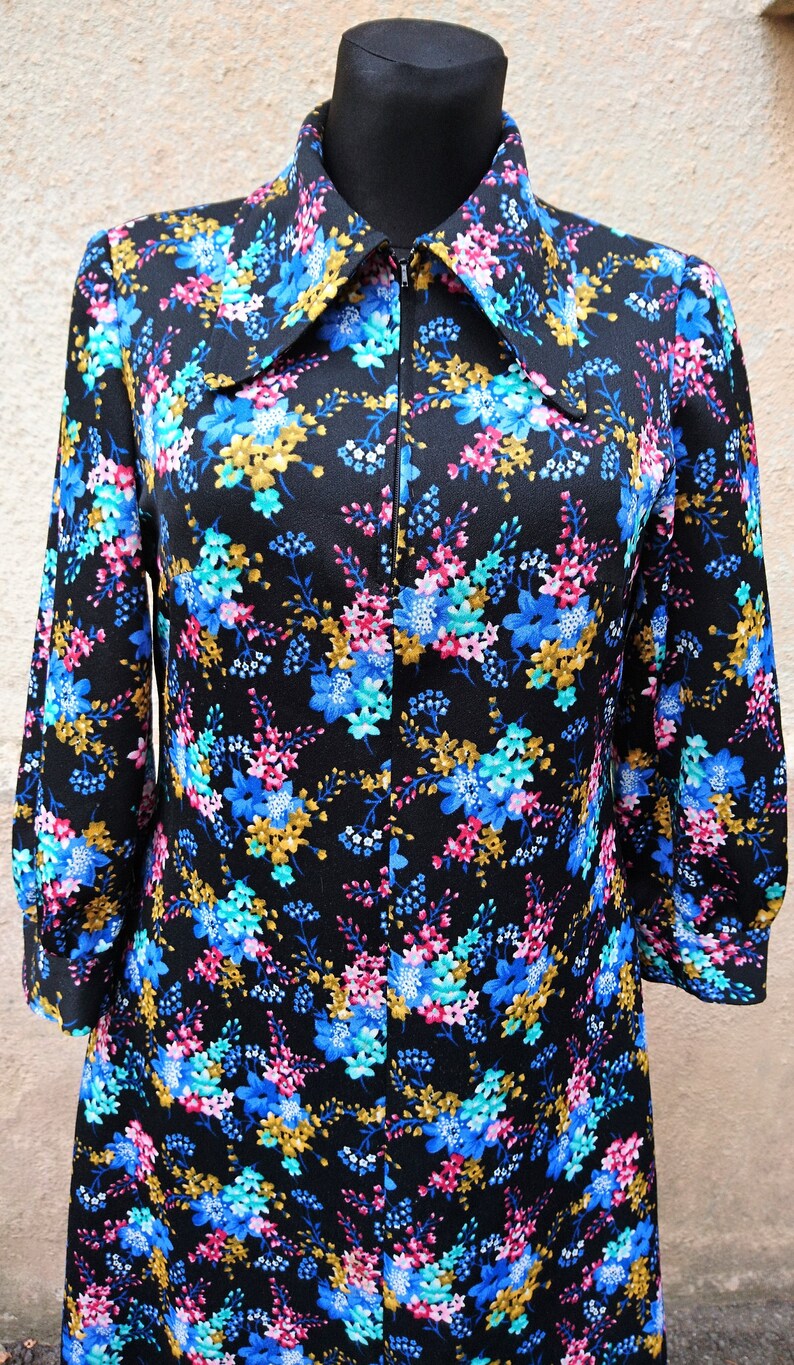 May include: A black long-sleeved dress with a floral print in shades of blue, pink, and gold. The dress has a zipper closure and a large collar.