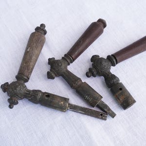 May include: Three antique door handles with wooden knobs and ornate metal accents. The handles are in various shades of brown and black.