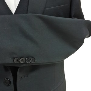 May include: A black suit with a white dress shirt and black vest. The suit jacket has four buttons on the sleeve and a pocket. The suit is a formal style.