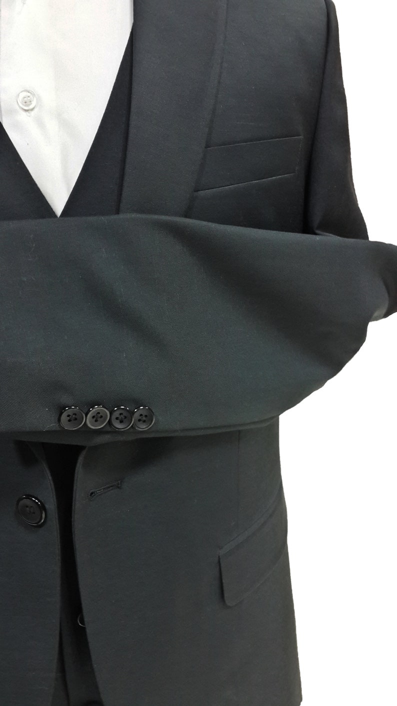 May include: A black suit with a white dress shirt and black vest. The suit jacket has four buttons on the sleeve and a pocket. The suit is a formal style.