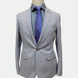 May include: A white and blue striped blazer with a single button closure. The blazer has a light blue shirt underneath with a purple tie.