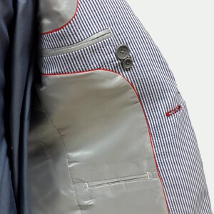 May include: A blue and white striped blazer with a red trim and a silver lining. The blazer has a pocket on the inside.