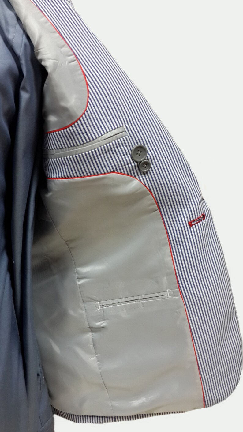 May include: A blue and white striped blazer with a red trim and a silver lining. The blazer has a pocket on the inside.