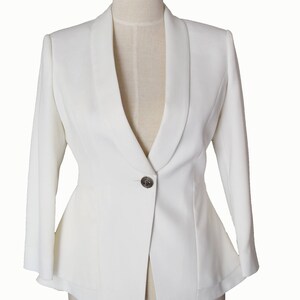 May include: A white blazer with a single button closure and a wide collar. The blazer has a fitted silhouette and long sleeves.