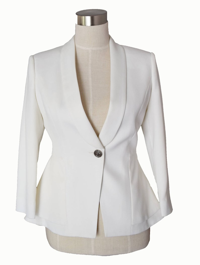 May include: A white blazer with a single button closure and a wide collar. The blazer has a fitted silhouette and long sleeves.