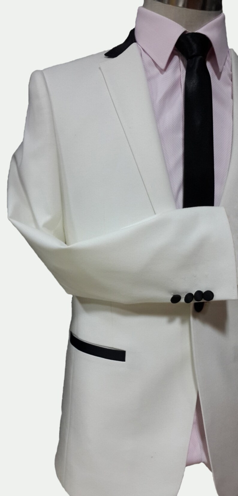 May include: A white tuxedo jacket with a black satin lapel and black buttons. The jacket has a black pocket trim and a single button closure.