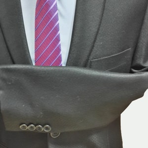 May include: A black suit jacket with a buttoned closure and a single button on the front. The jacket has a striped purple and pink tie with a white shirt underneath.