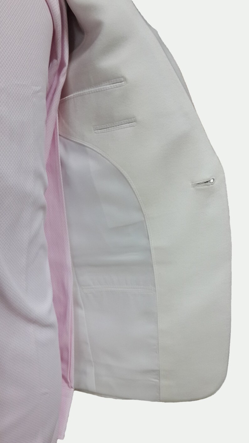 May include: A white blazer with a single button closure and a pocket on the inside. The blazer is unbuttoned and the inside lining is visible.