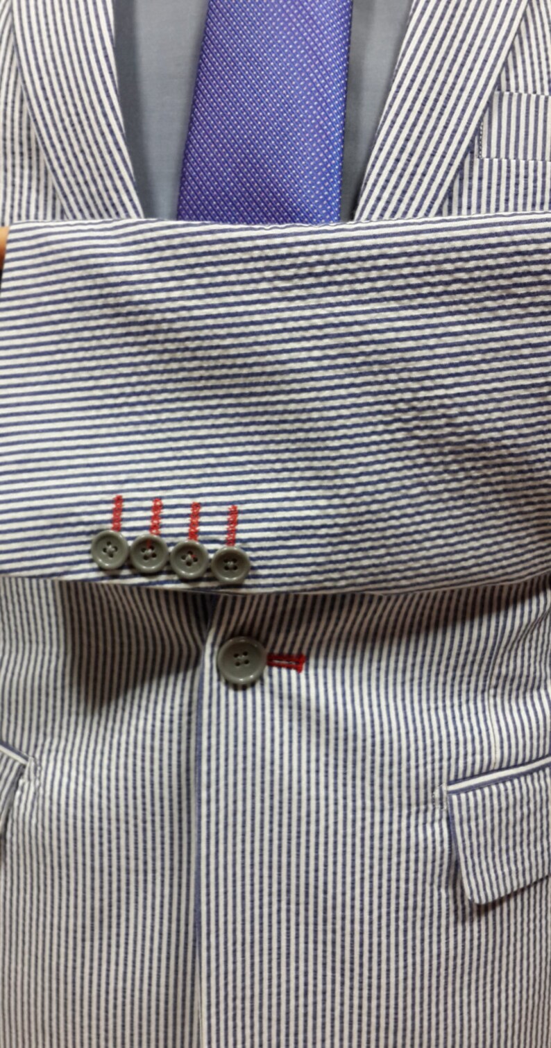 May include: A striped blue and white blazer with a blue patterned tie and four buttons on the left side of the jacket.