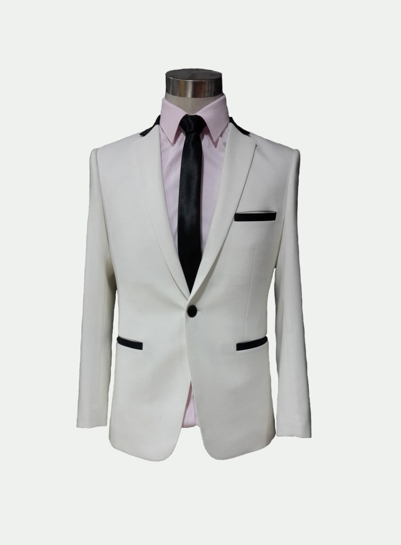 May include: A white suit jacket with black trim and a single button closure. The jacket is worn over a pink dress shirt with a black tie.