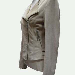 May include: A beige suede jacket with a zipper closure and a collar that can be worn up or down.