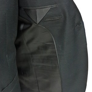 May include: A black blazer with a satin lapel and interior lining. The inside of the jacket reveals a pocket and a tailored design. The blazer is made of a dark, possibly wool, fabric.