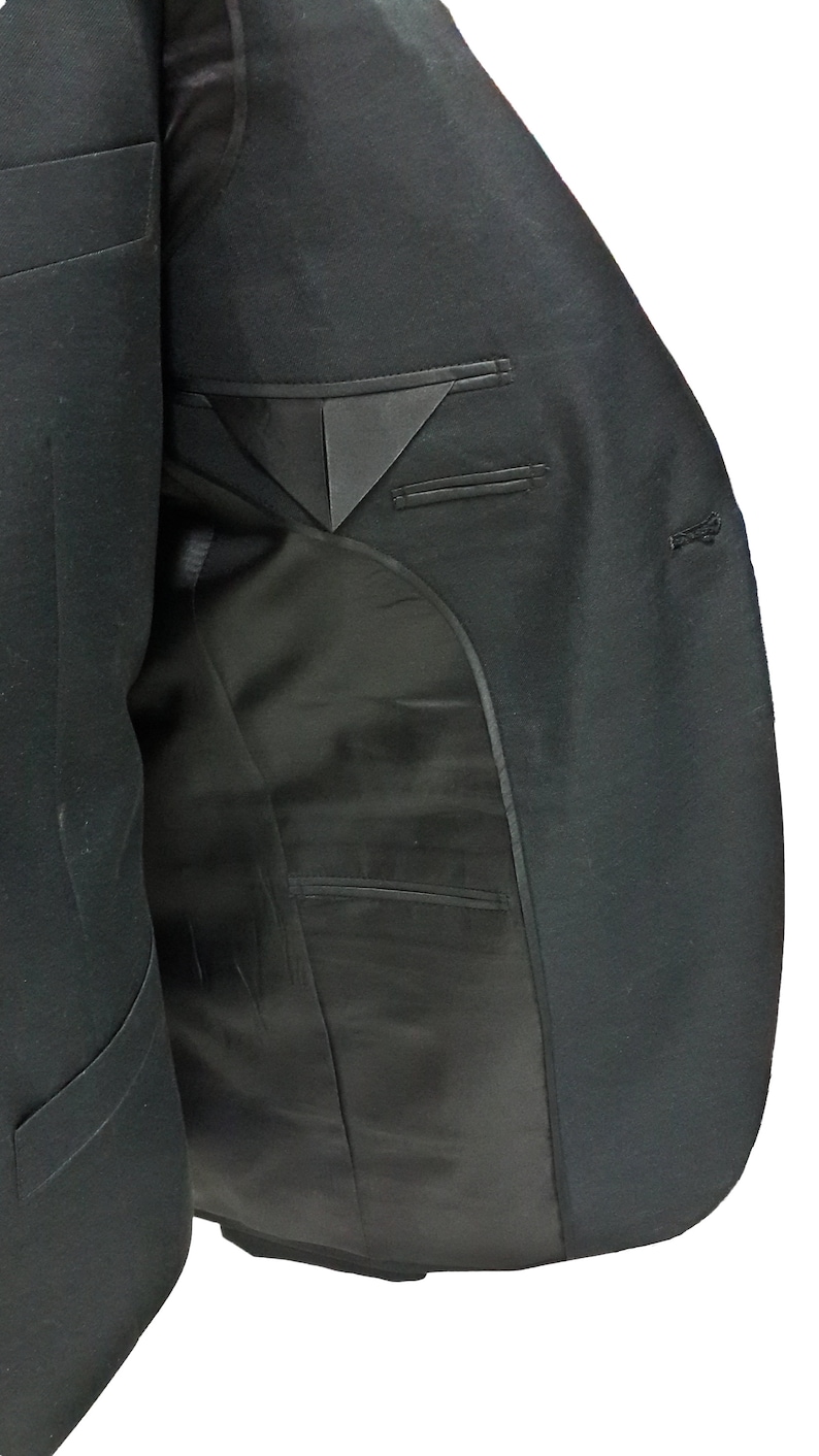 May include: A black blazer with a satin lapel and interior lining. The inside of the jacket reveals a pocket and a tailored design. The blazer is made of a dark, possibly wool, fabric.