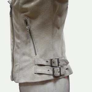 May include: A light beige suede jacket with a zipper closure and a buckle detail at the bottom.