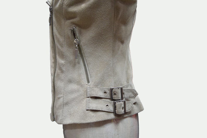 May include: A light beige suede jacket with a zipper closure and a buckle detail at the bottom.