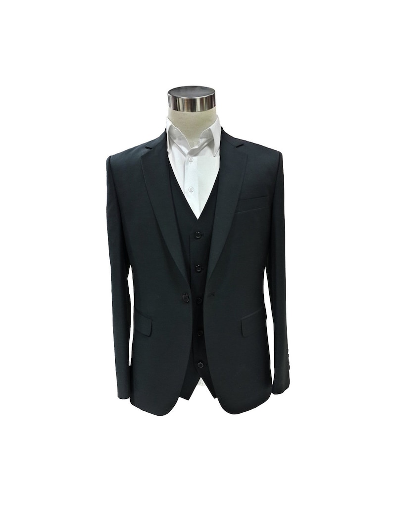 May include: A dark charcoal gray three-piece suit displayed on a mannequin. The suit includes a jacket, vest, and dress pants. A white collared shirt is visible beneath the suit jacket. The suit is tailored with a classic fit.