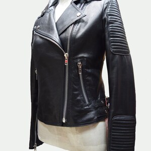 May include: Black leather motorcycle jacket with a zipper closure, a stand-up collar, and zippered pockets. The jacket has a quilted detail on the sleeves.