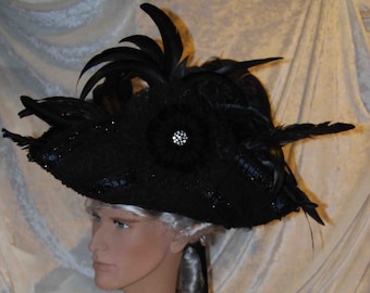 May include: A black wide-brimmed hat with a large black feather and a black flower with a rhinestone center.