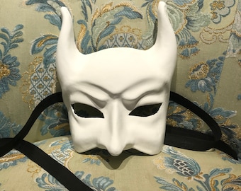 May include: White masquerade mask with horns and eye holes, on a floral patterned fabric background.