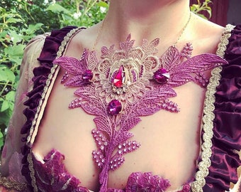 Op de afbeelding: Een delicate paarse en gouden kanten ketting met een bloemmotief en glinsterende roze en heldere strass steentjes.