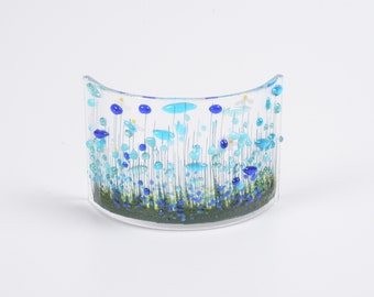 May include: A glass art piece with a curved shape, featuring a design of blue, green, and white flowers on a clear background.