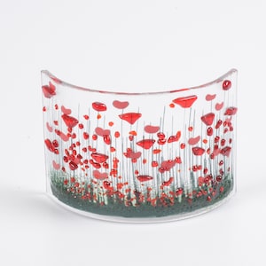 May include: A clear glass vase with a curved shape features a design of red poppies on thin stems. The bottom of the vase has a green layer representing grass.