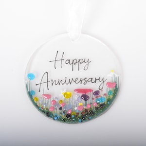 May include: Round glass bauble with the text "Happy Anniversary" in black script. The bauble is filled with colourful glass beads and glitter, resembling a field of flowers.