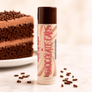 Könnte beinhalten: Ein zylindrischer Lippenbalsamstift mit dunkelbrauner Kappe und beigem Etikett mit braunen Wirbellinien. Der Text lautet Sheer Lip Balm in Chocolate Cake mit einem Nettogewicht von 4,25 g. Das Etikett enthält einen hellblauen Akzentstreifen.