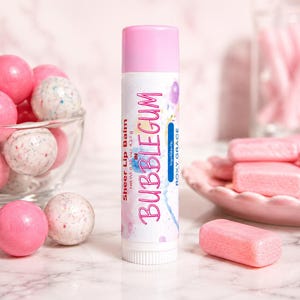 May include: A cylindrical lip balm tube with a pink cap and white label featuring the text Sheer Lip Balm, BUBBLEGUM, and Roxy Grace. The label includes watercolor accents and states a net weight of 0.15 oz / 4.25 g.
