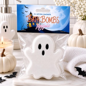 May include: A white ghost-shaped bath bomb in a clear plastic bag with a header card featuring a haunted house, bats, and the text "All Natural Handmade Bath Bombs" and "Posy Grace and Company" in orange and pink script lettering.