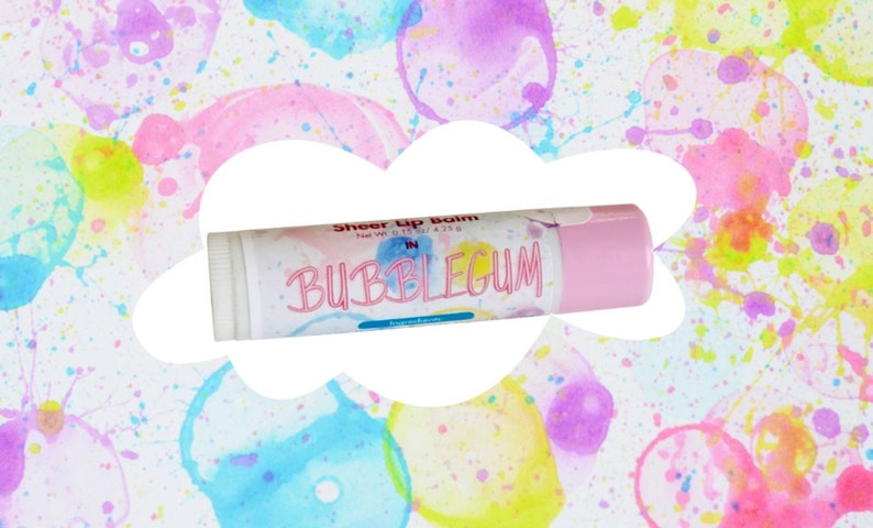 May include: A cylindrical lip balm tube with a light pink cap and a white label featuring the text Sheer Lip Balm, Net Wt. 0.15 oz / 4.25 g, and BUBBLEGUM in pink lettering. The label has a colorful watercolor splatter pattern.