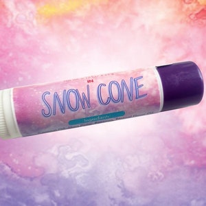 Puede incluir: Un tubo cil&iacute;ndrico de b&aacute;lsamo labial con tapa morada y base blanca. La etiqueta presenta un fondo de acuarela rosa y morado con el texto "SNOW CONE" en letras azules, junto a un peque&ntilde;o rect&aacute;ngulo color verde azulado etiquetado "Ingredients".